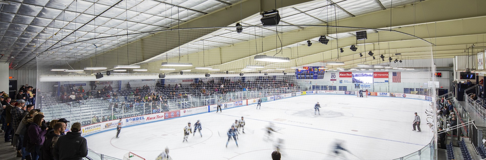 Wide shot showing ice hockey game and its fans on either side